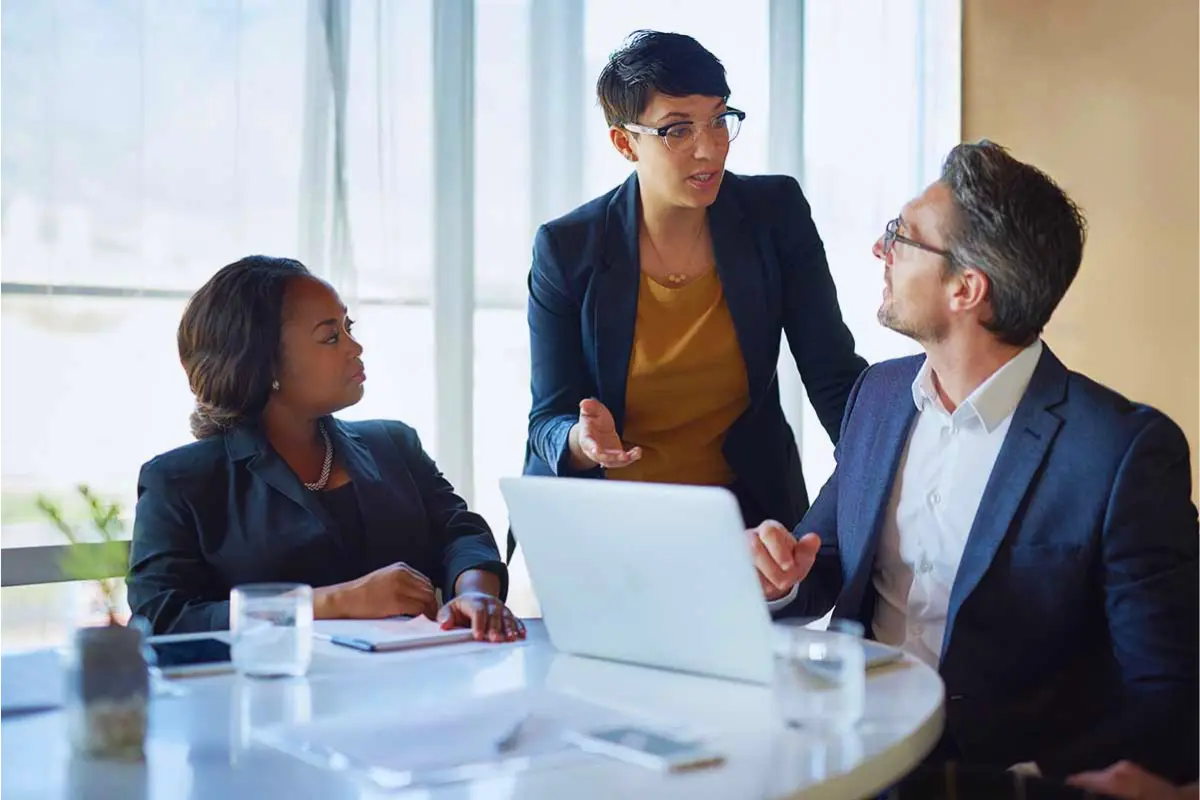 Three business professionals discussing management decisions around a laptop in a meeting.